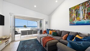 Een woonkamer met een grijze bank, kleurrijke kussens, een blauw kamerkleed en een schilderij aan de muur.