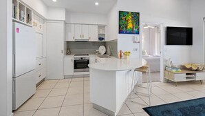 Een moderne keuken met witte kasten, een centraal kookeiland en een eethoek met televisie en zitplaatsen.