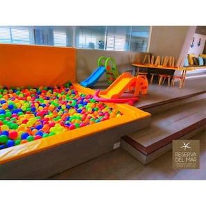 Zona de juegos infantiles con piscina de pelotas y toboganes.