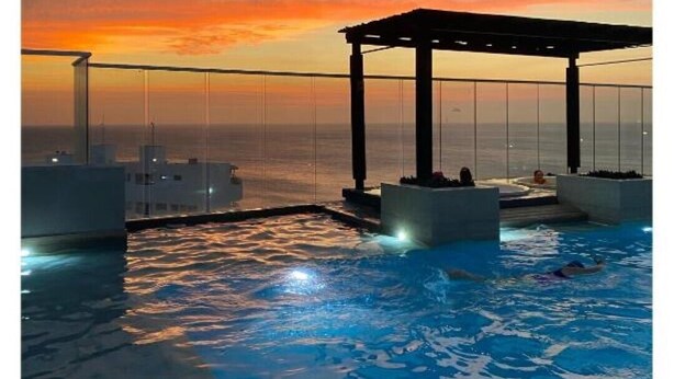 En infinitypool med utsikt över solnedgången, ett avskärmat sittområde och ett glasräcke.