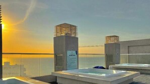 En takterrass med bubbelpooler och utsikt över solnedgången över havet.