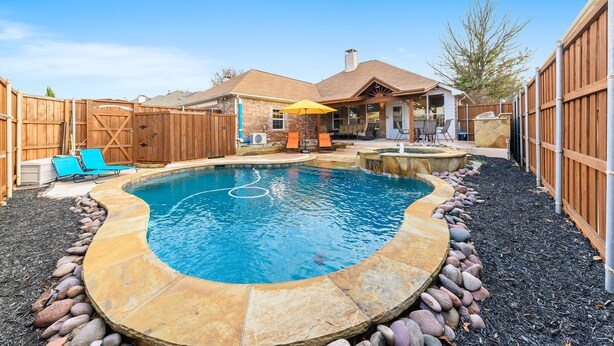 Un jardin avec une piscine, une bordure en pierre et une clôture en bois.