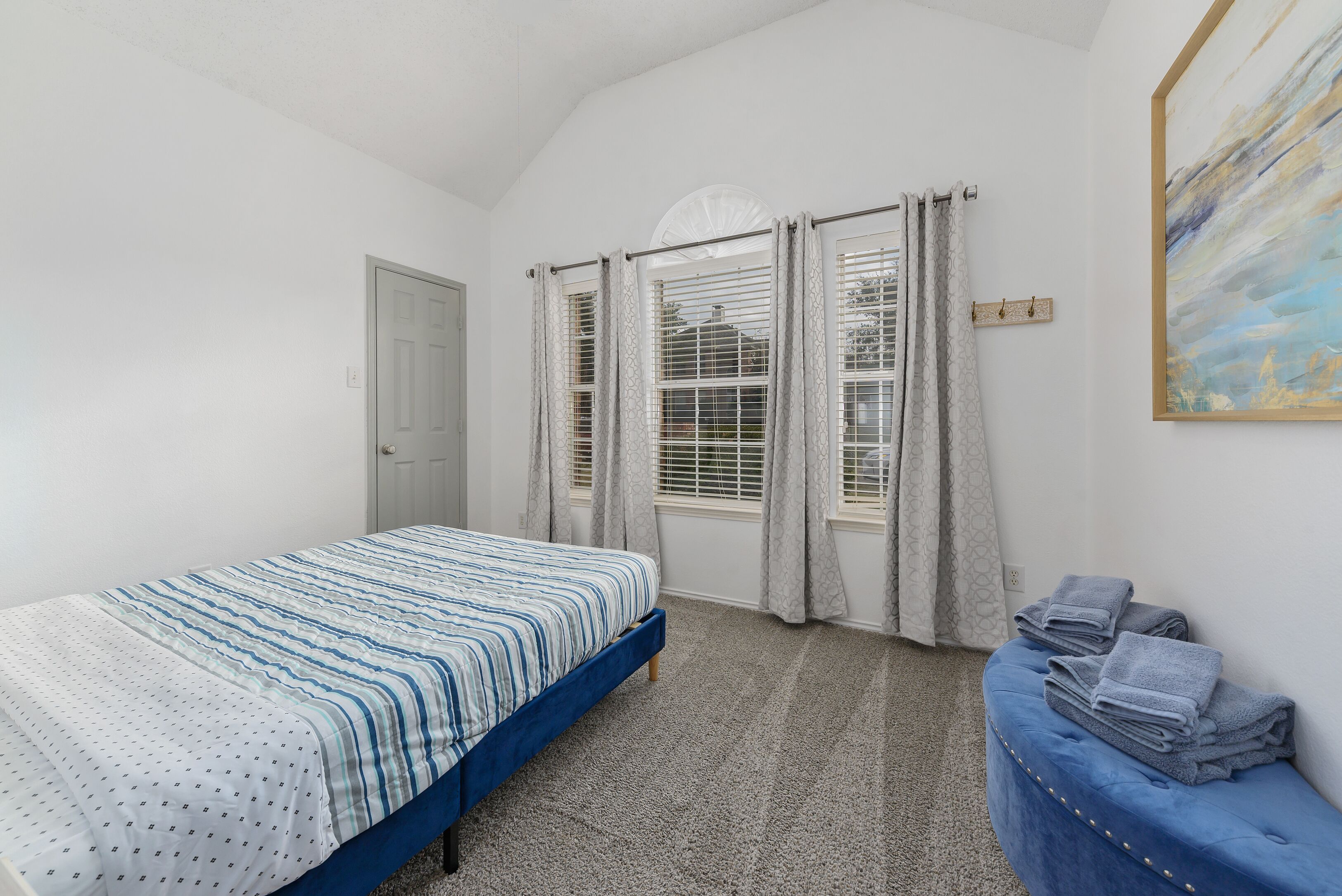 A bedroom with a bed, a blue bench, and a painting on the wall.