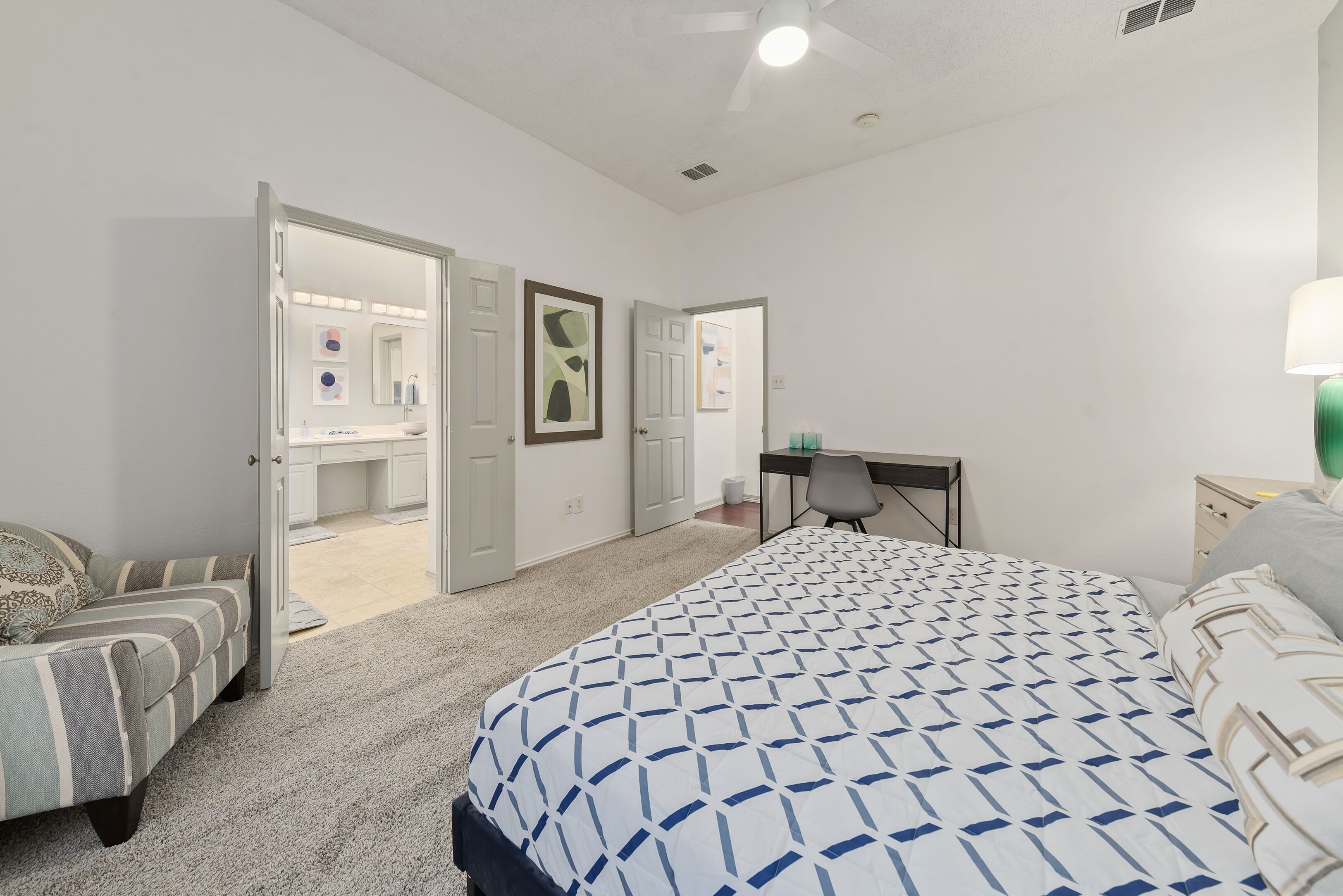 A bedroom with a bed, a desk, and a chair. There are two doors leading to other rooms.