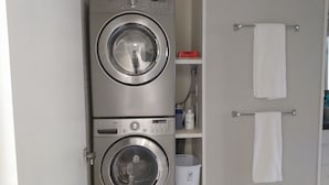 A laundry room with two stacked front-loading washing machines, a white trash bin, and a towel rack with two white towels. - Family Friendly Fully Renovated Quiet House  (Dresden)
