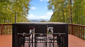 A deck with a table and chairs, surrounded by trees and a mountain view. - Comfy Lodge with Stunning Mountain Views (Waynesville)