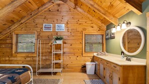 A cabin with a loft bedroom, a bathroom with a sink and mirror, and wooden walls. - Comfy Lodge with Stunning Mountain Views (Waynesville)