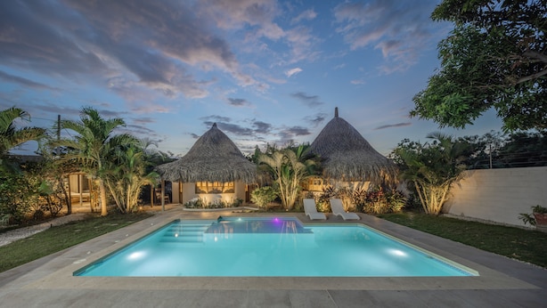 A pool area with two thatched-roof structures, surrounded by tropical vegetation. - Villa el Oasis, luxurious Santa Marta getaway (rodadero)