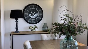Uma mesa de jantar com um vaso de flores, um relógio na parede e um abajur.