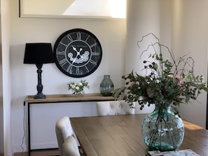 A dining table with a vase of flowers, a wall clock, and a lamp.