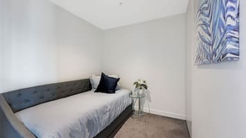 A bedroom with a bed, a small round table with a plant, and a painting on the wall.