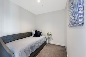 A bedroom with a bed, a small round table with a plant, and a painting on the wall.