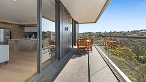 Uma varanda moderna com vista para uma paisagem montanhosa, área de refeições com móveis de madeira e cozinha com geladeira embutida.