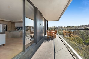 A modern balcony with a view of a hilly landscape, a dining area with wooden furniture, and a kitchen with a built-in refrigerator.