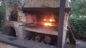 A stone-built outdoor pizza oven with a fire burning inside, surrounded by logs and a rustic setting. - Apartment Ortensia 1 Bedroom, Living Room,bathroom (Monte Castello di Vibio)