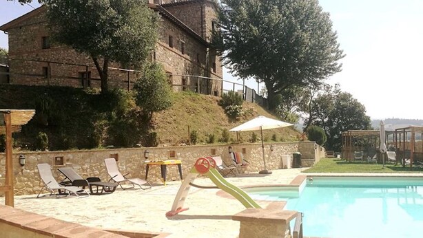 A pool area with lounge chairs, a slide, and a stone building in the background. - Apartment Ortensia 1 Bedroom, Living Room,bathroom (Monte Castello di Vibio)