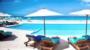 Un espace piscine avec des chaises longues et des parasols, une vue dégagée sur l’océan et une plage de sable.