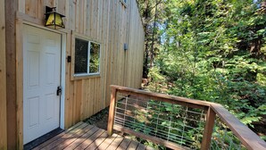 A wooden cabin with a white door, two windows, and a small porch with a wooden railing. - Beautiful cottage, close to beach (Port Orford)