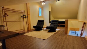 A room with a wooden floor, a black chair, a sofa, a small table, and a window with a view. - Beautiful cottage, close to beach (Port Orford)