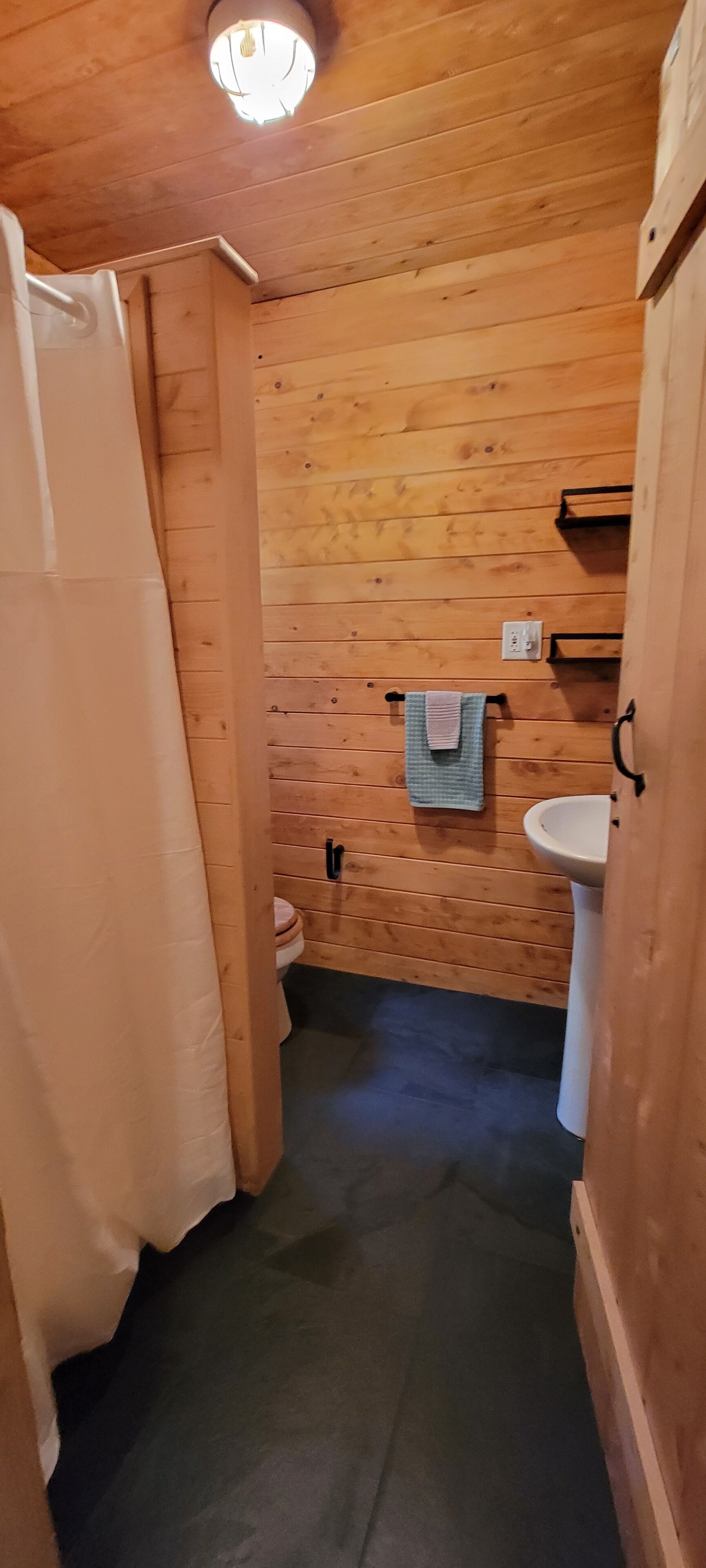 Un baño con paneles de madera, un inodoro, un lavamanos y un perchero para toallas.