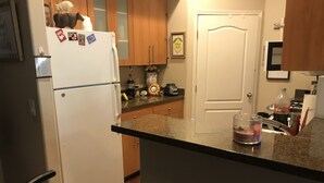 Une cuisine équipée d’un réfrigérateur, de meubles de rangement en bois, d’une porte et d’un plan de travail sur lequel se trouvent divers objets.