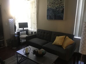 Ein Wohnzimmer mit grauem Sofa, einem kleinen Tisch mit Kerze und einem Baumgemälde an der Wand.