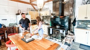 Una cocina con una gran mesa de madera, sillas rojas, una estufa negra y armarios blancos.