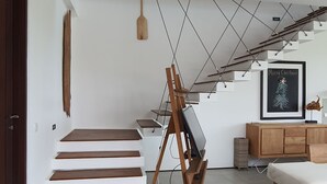 Een modern interieur met een trap, een houten schildersezel, een ingelijste afbeelding en een minimalistische zithoek.