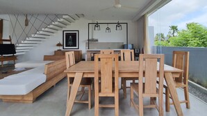 Een moderne woonkamer met een houten eettafel en stoelen, een bank, een trap en een keukenhoek.