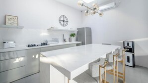 A modern kitchen with a central island, white cabinetry, a clock, and a coffee machine. - Mile Stone Villa (Jimbaran)