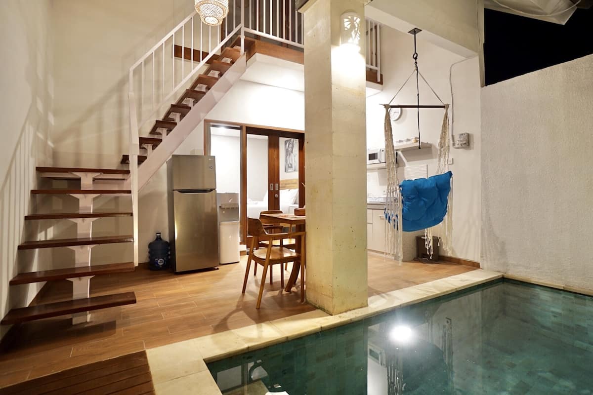 A spacious indoor area with a wooden staircase, a dining table with chairs, a hanging light fixture, and a pool.