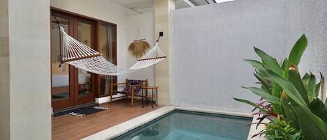 Un espace piscine avec un hamac, une terrasse en bois et une vue sur l’intérieur.