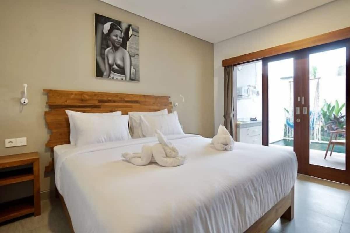 A bedroom with a wooden headboard, a bed with white linens, and a painting on the wall.