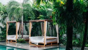 Two wooden canopy beds by a poolside, surrounded by lush tropical plants. - The Kamare by Zuzu (Tibubeneng)