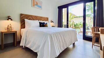 Habitación de hotel con una cama grande, cabecera de madera, mesita de noche con lámpara y vista al exterior por una puerta corrediza de vidrio.