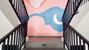 A staircase with a mural of a sunset and moon. - The Kamare by Zuzu (Tibubeneng)