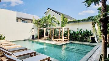 Un área de piscina con sillones de descanso, un pabellón de madera y plantas tropicales.