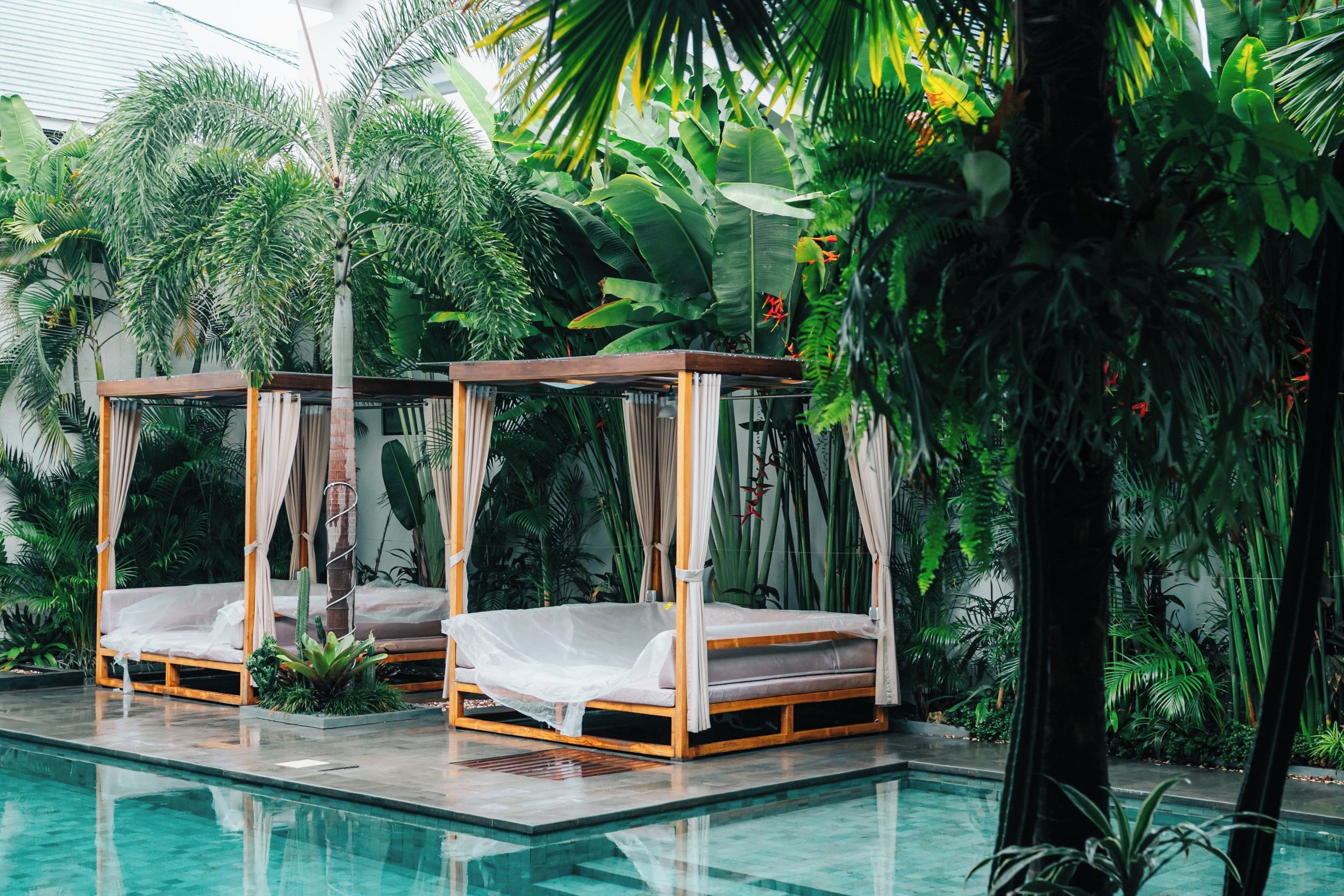 Un espace aménagé au bord de la piscine, avec deux lits à baldaquin en bois et une végétation tropicale luxuriante.