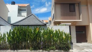 A modern residential building with a flat roof, a balcony, and a gated entrance. - Little Nuts Villa (Jimbaran)