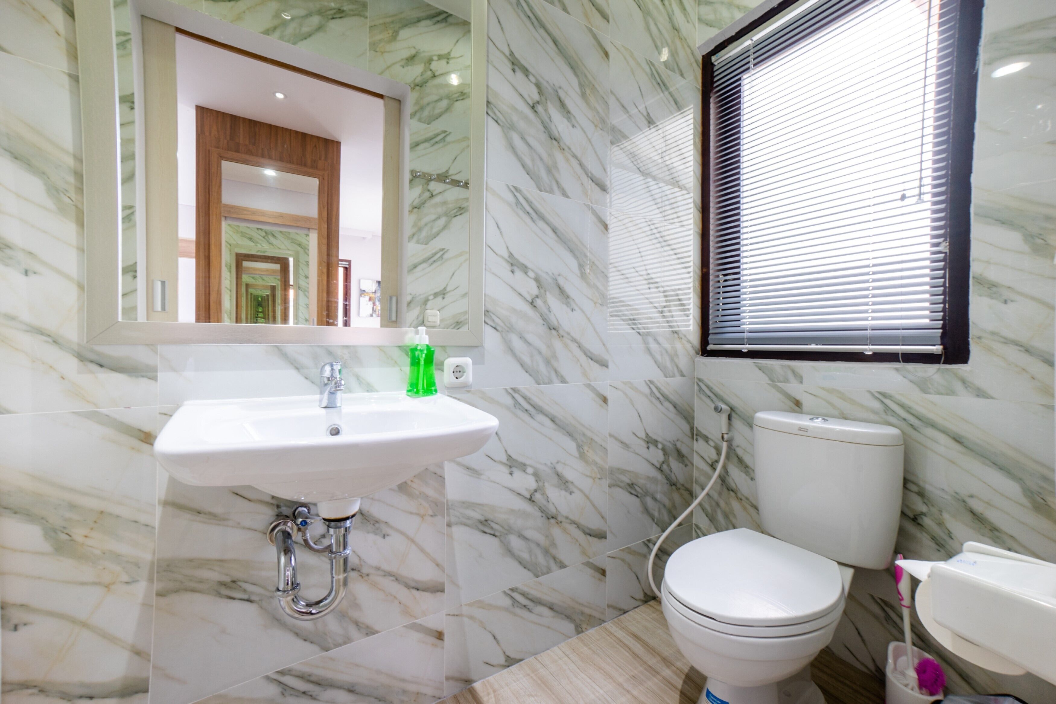 A bathroom with a marble sink, toilet, and a window with blinds.