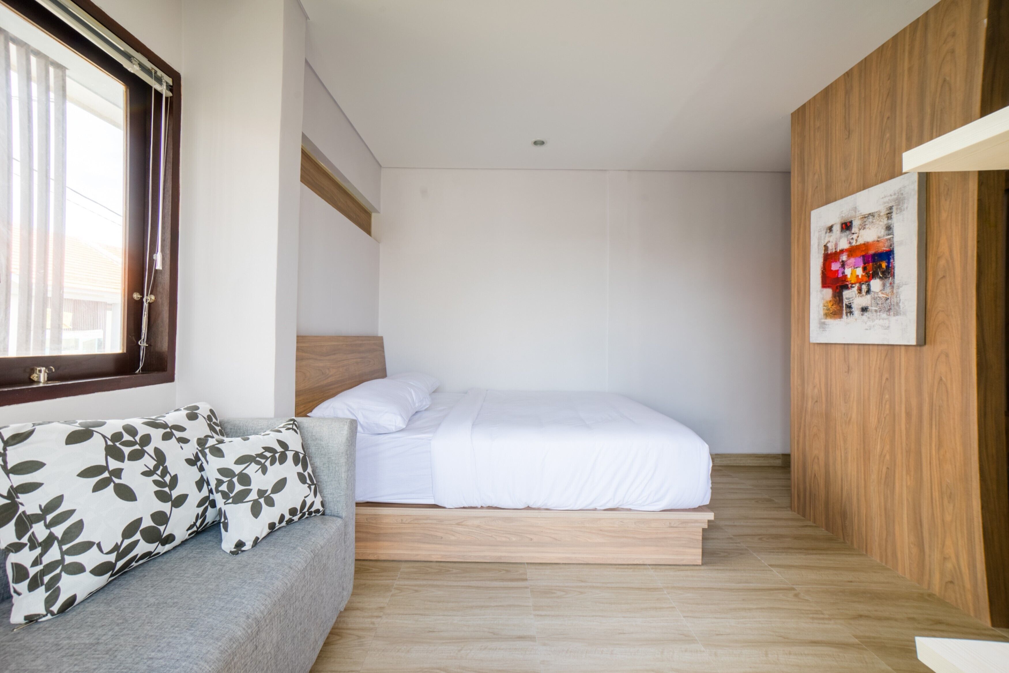Un dormitorio con cama, un sofá gris con cojines estampados, suelo de madera y un panel de pared de madera.