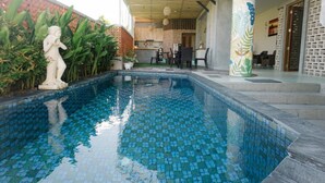 A swimming pool with mosaic tiles, a statue, and a building with a covered patio area. - Natura Nusa Dua (Nusa Dua)