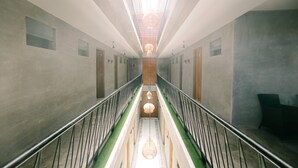 A long, narrow hallway with a central walkway, flanked by walls with small windows and a metal railing. - Natura Nusa Dua (Nusa Dua)