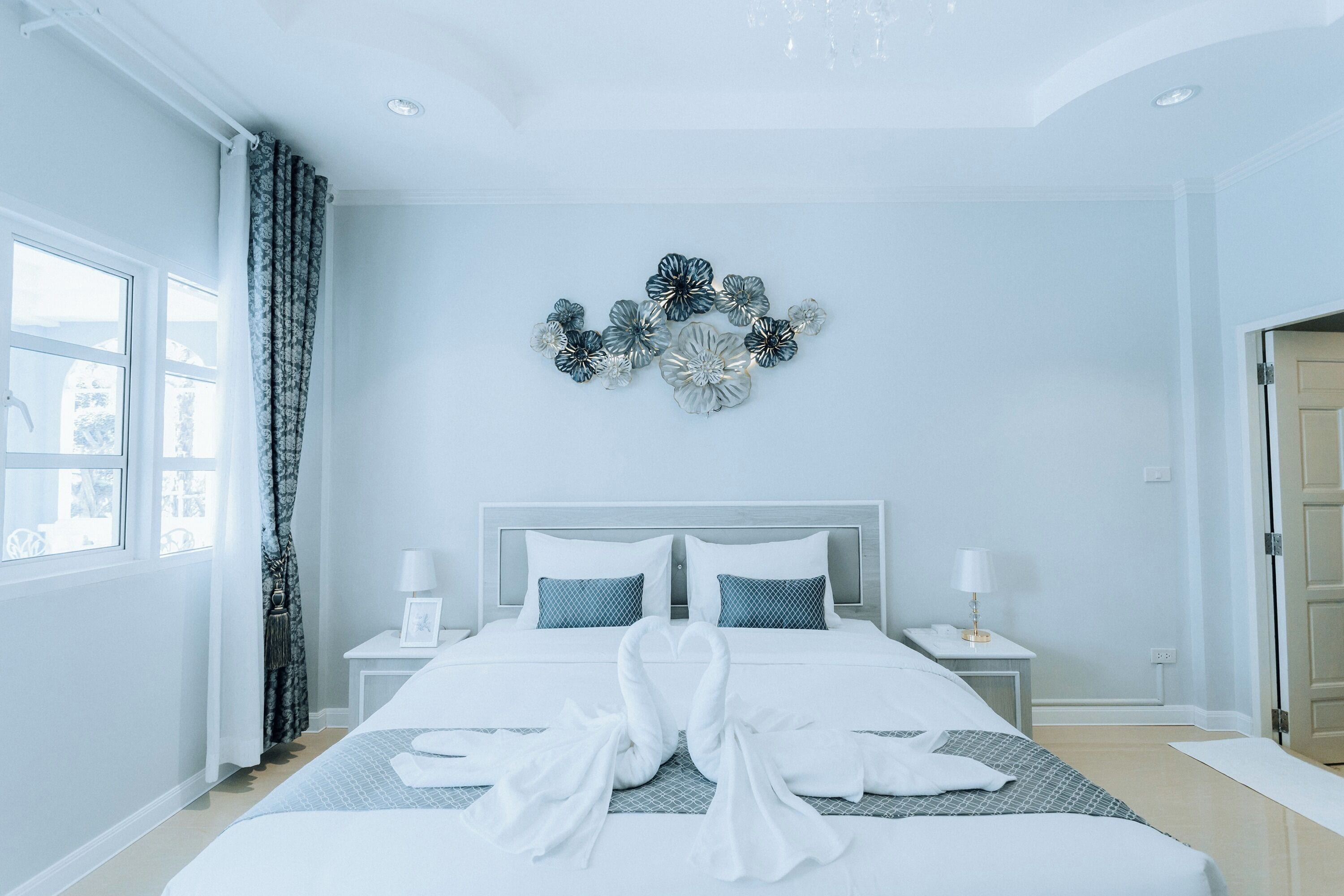 A hotel room with a large bed, two bedside tables, a wall-mounted decorative piece, and a view through the window.