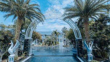 Una entrada imponente con un arco blanco, palmeras y un edificio grande al fondo.