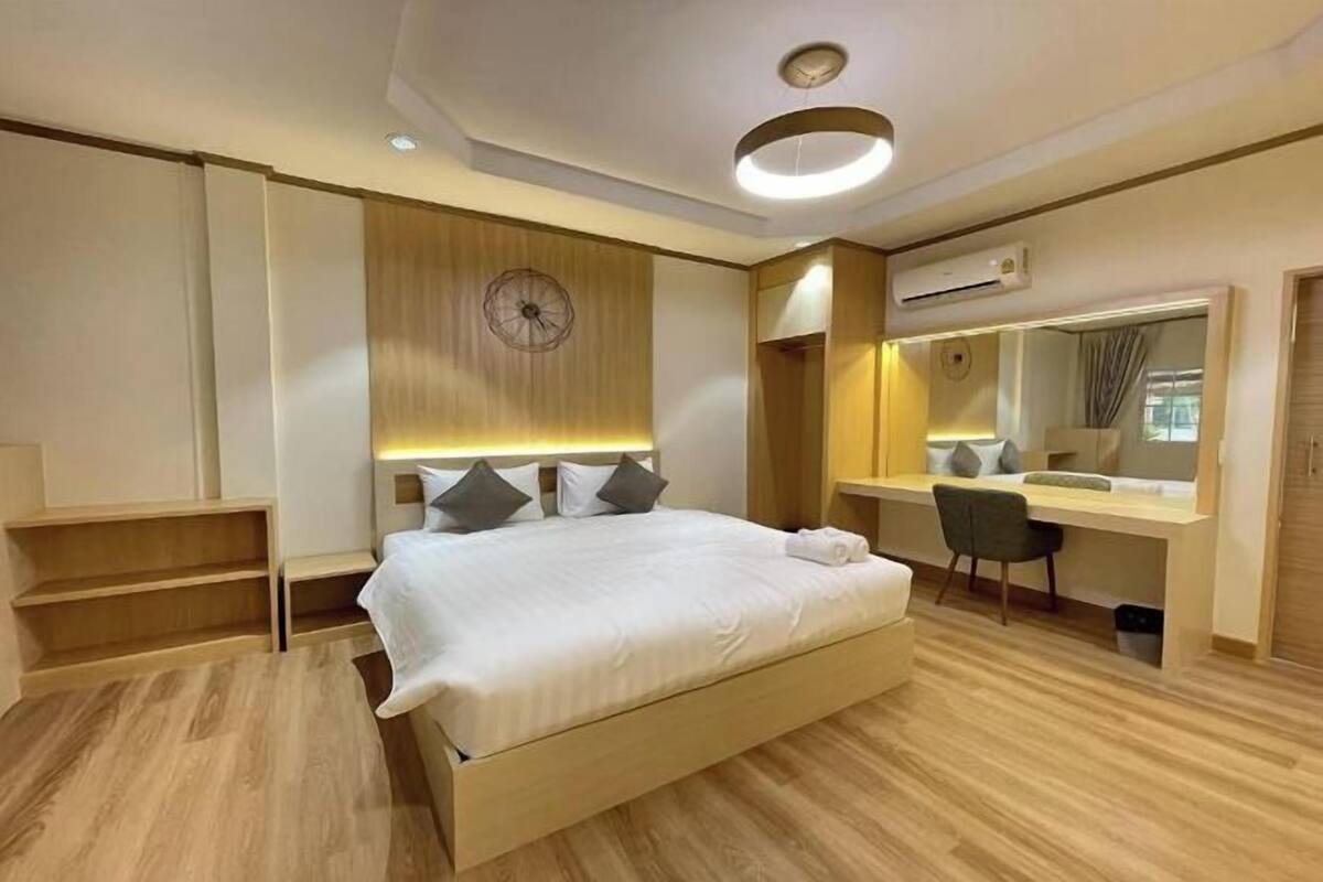 A modern hotel room with a large bed, a desk, a mirror, and a clock on the wall.