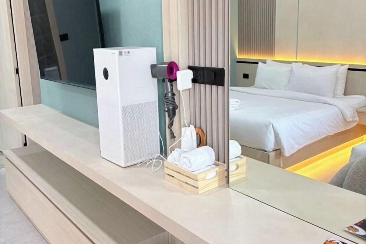 A hotel room with a bed, a mirror, a white speaker, and a towel rack.