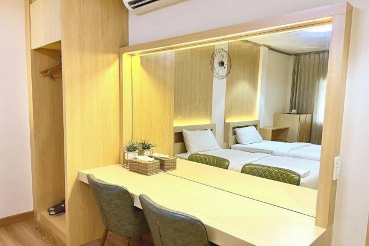 A hotel room with a bed, a desk, chairs, a mirror, and a clock.