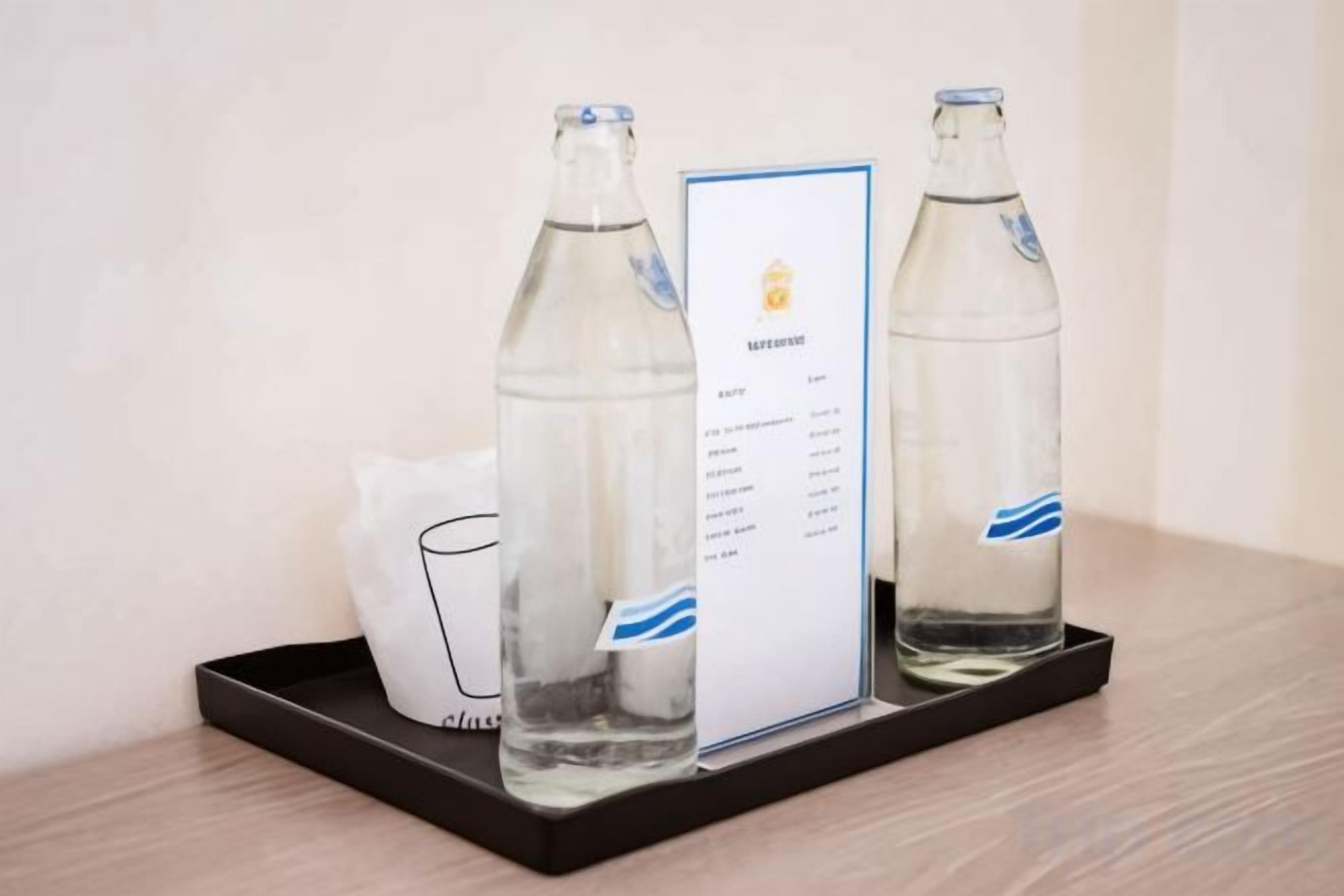 Dos botellas de vidrio transparente sobre una bandeja con una tarjeta de menú a un lado.