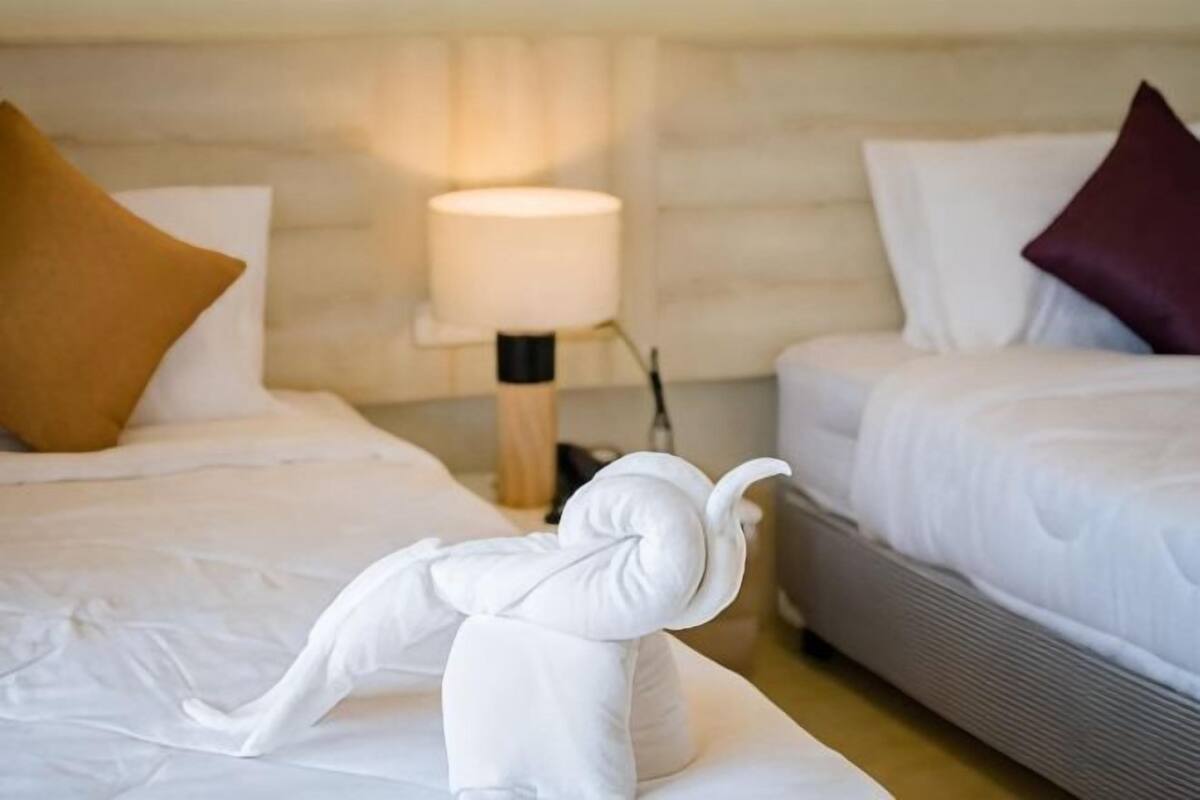 A hotel room with two beds, a nightstand with a lamp, and a towel sculpture on the floor.
